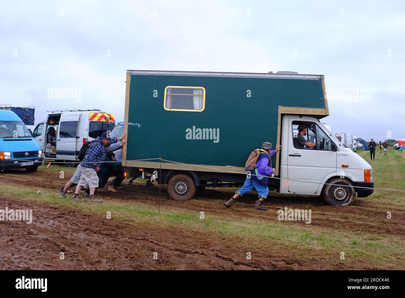 Persone che spingono un camion, un veicolo, bloccati in un campo fangoso al Tropical Pressure Festival in Cornovaglia, Regno Unito Foto Stock