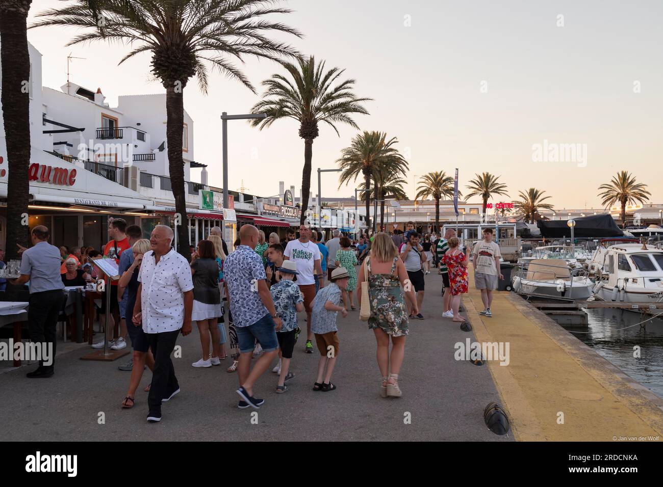 I turisti passeggeranno davanti agli accoglienti ristoranti sul porto nella località balneare di Cala en Bosc sull'isola spagnola di Minorca. Foto Stock