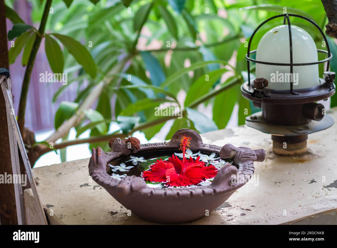 acqua santa spirituale con fiore di ibisco custodito per gli uccelli all'ingresso di casa da una diversa angolazione Foto Stock