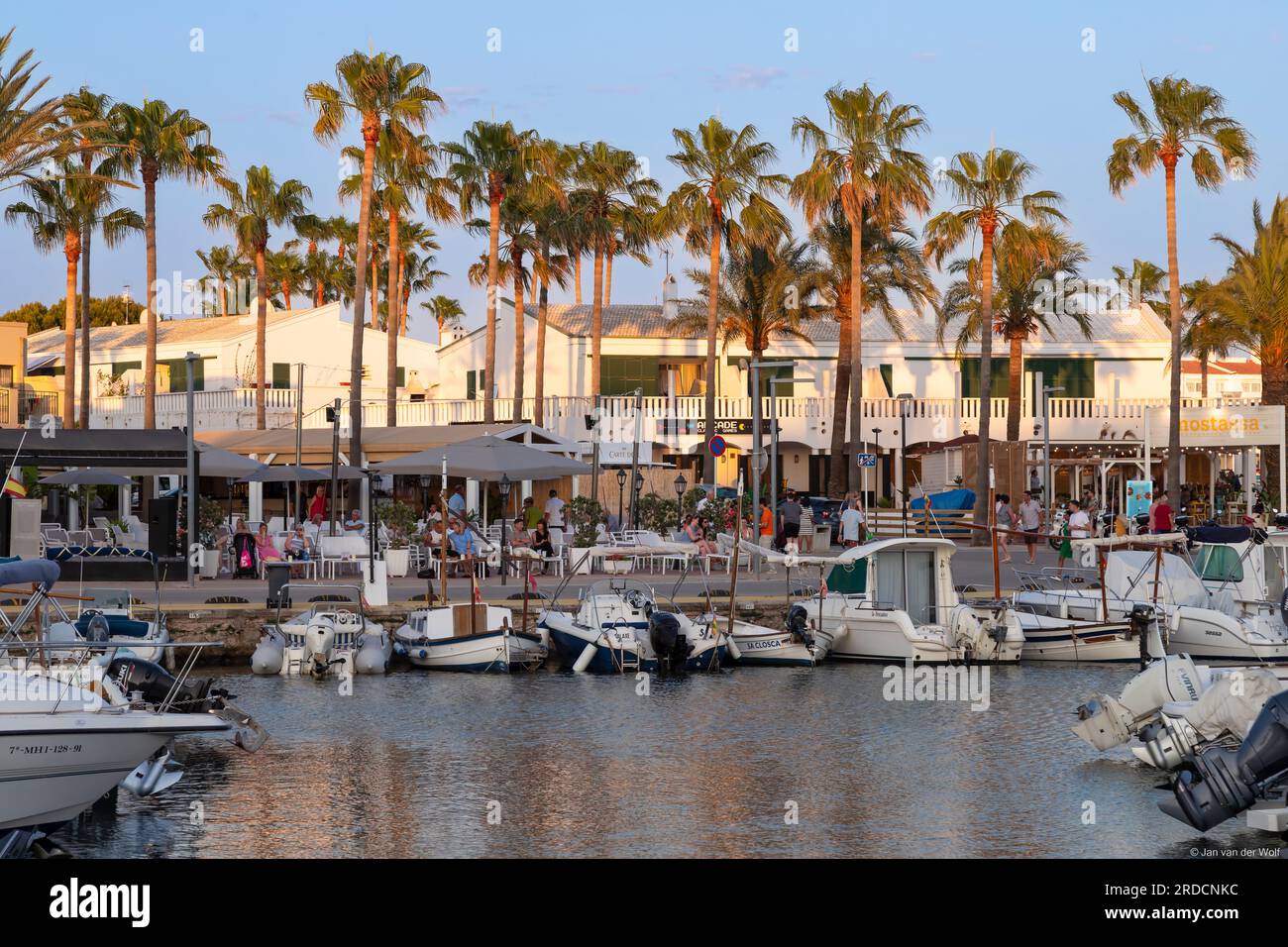 I turisti si godono le terrazze lungo il porto nella località di Cala en Bosc sull'isola spagnola di Minorca. Foto Stock