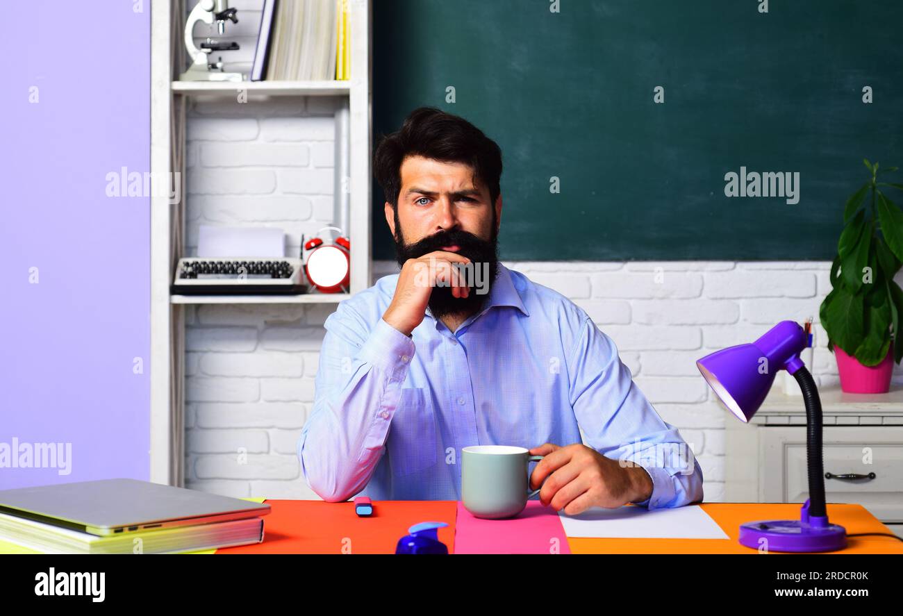 Serio insegnante maschio che beve caffè in classe. Insegnante o professore universitario sul posto di lavoro che beve una tazza di tè. Insegnante di scuola barbuto uomo che ha Foto Stock