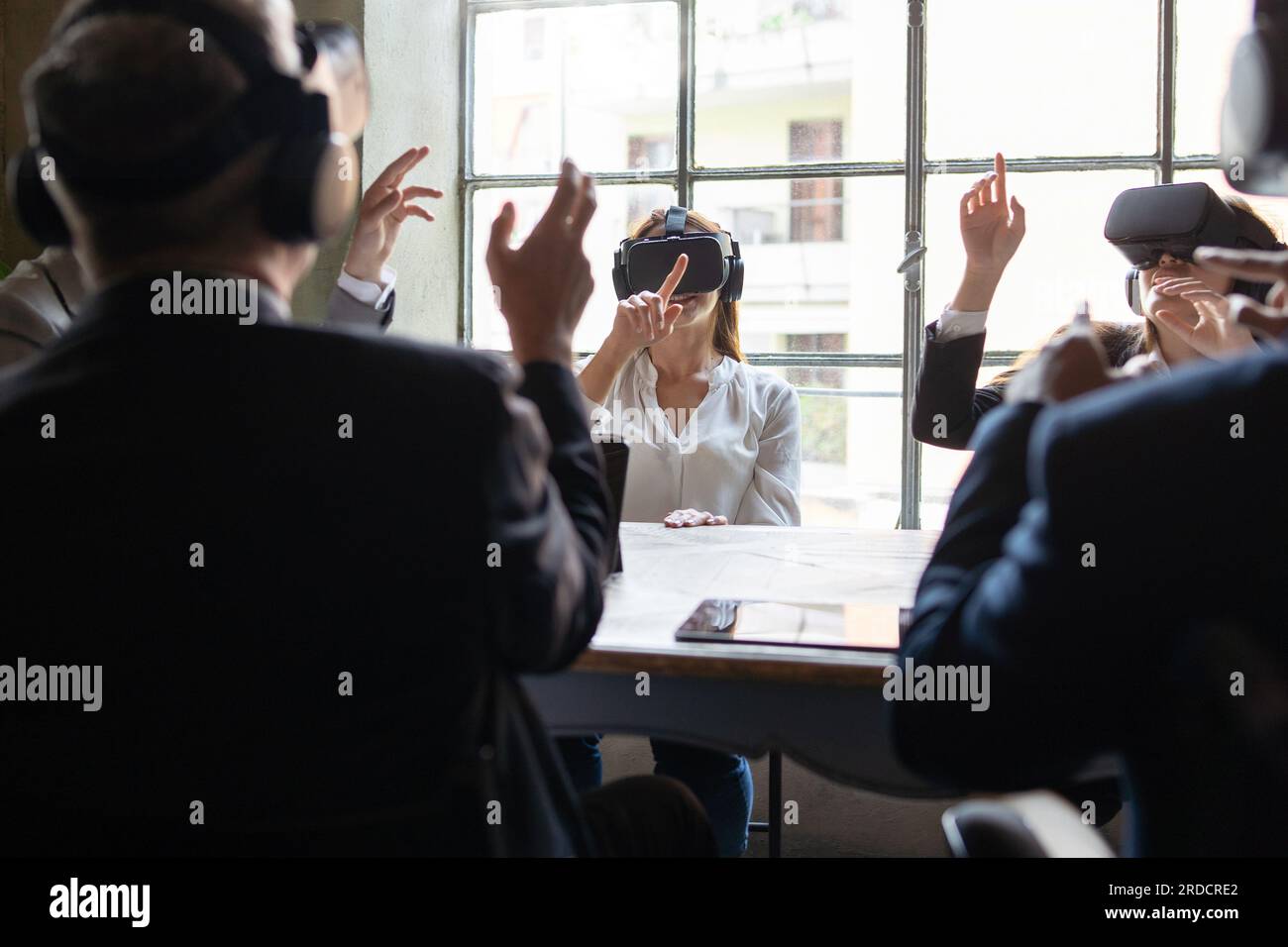 Team diversificato di colleghi in una riunione di lavoro in realtà virtuale in un ufficio. Tutti indossano occhiali VR e gestano con le mani. Foto Stock