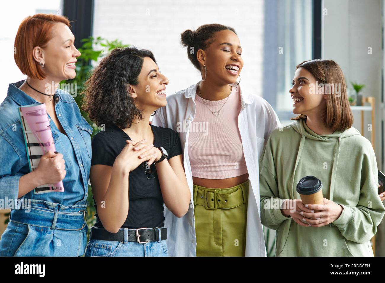 giovane e felice donna con un caffè per andare a guardare eleganti amici multietnici femminili in piedi e ridere nel club di interesse femminile, sostegno reciproco, così Foto Stock