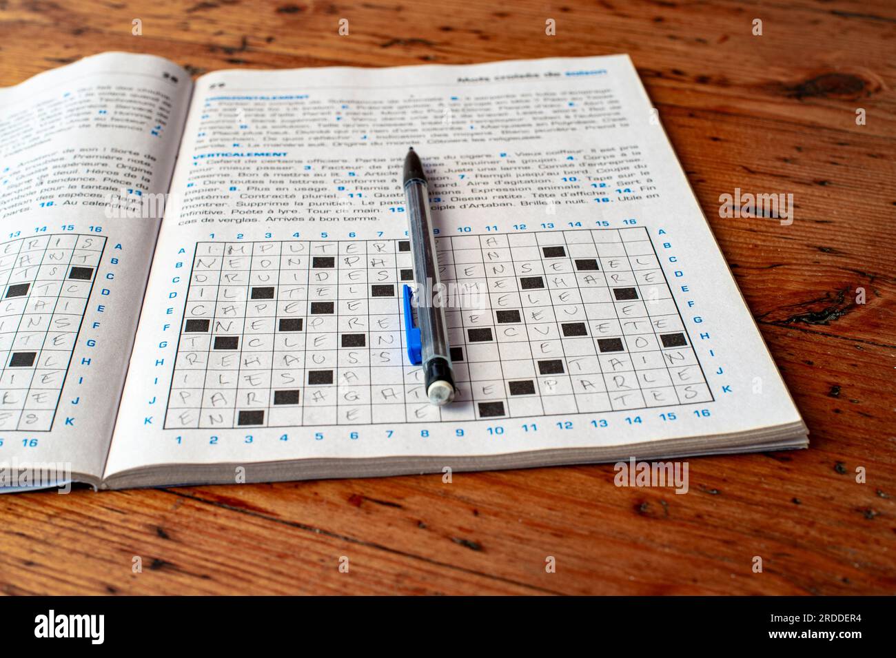 Libro degli esercizi del puzzle della parola crociata francese. Il libro si trova su un tavolo di legno di colore rosso. La matita si trova sul notebook. Foto Stock