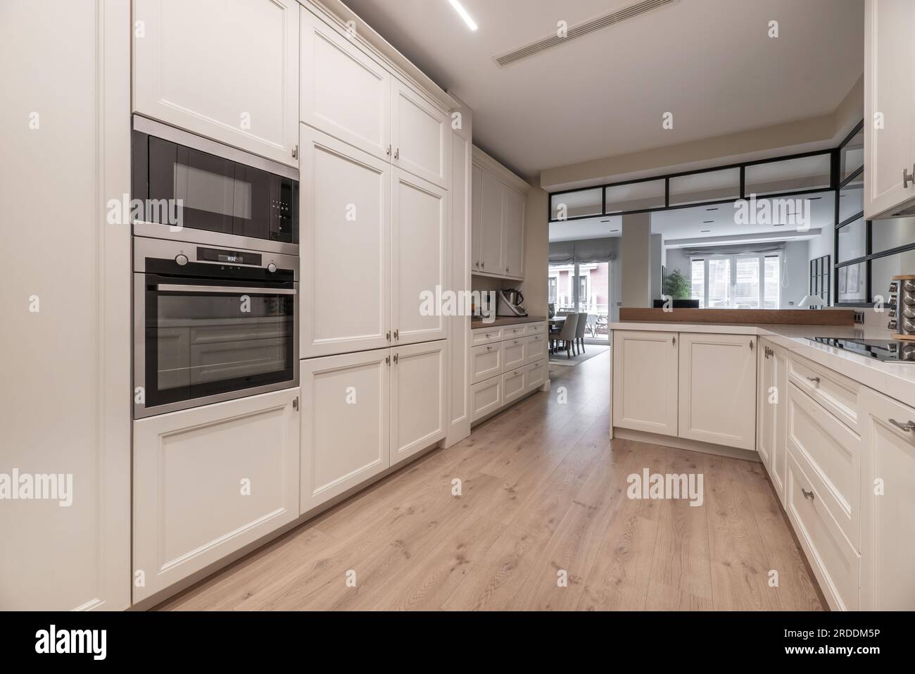 Una spaziosa cucina con pareti ricoperte di armadi di legno bianco da pavimento a soffitto con pavimenti di legno chiaro Foto Stock