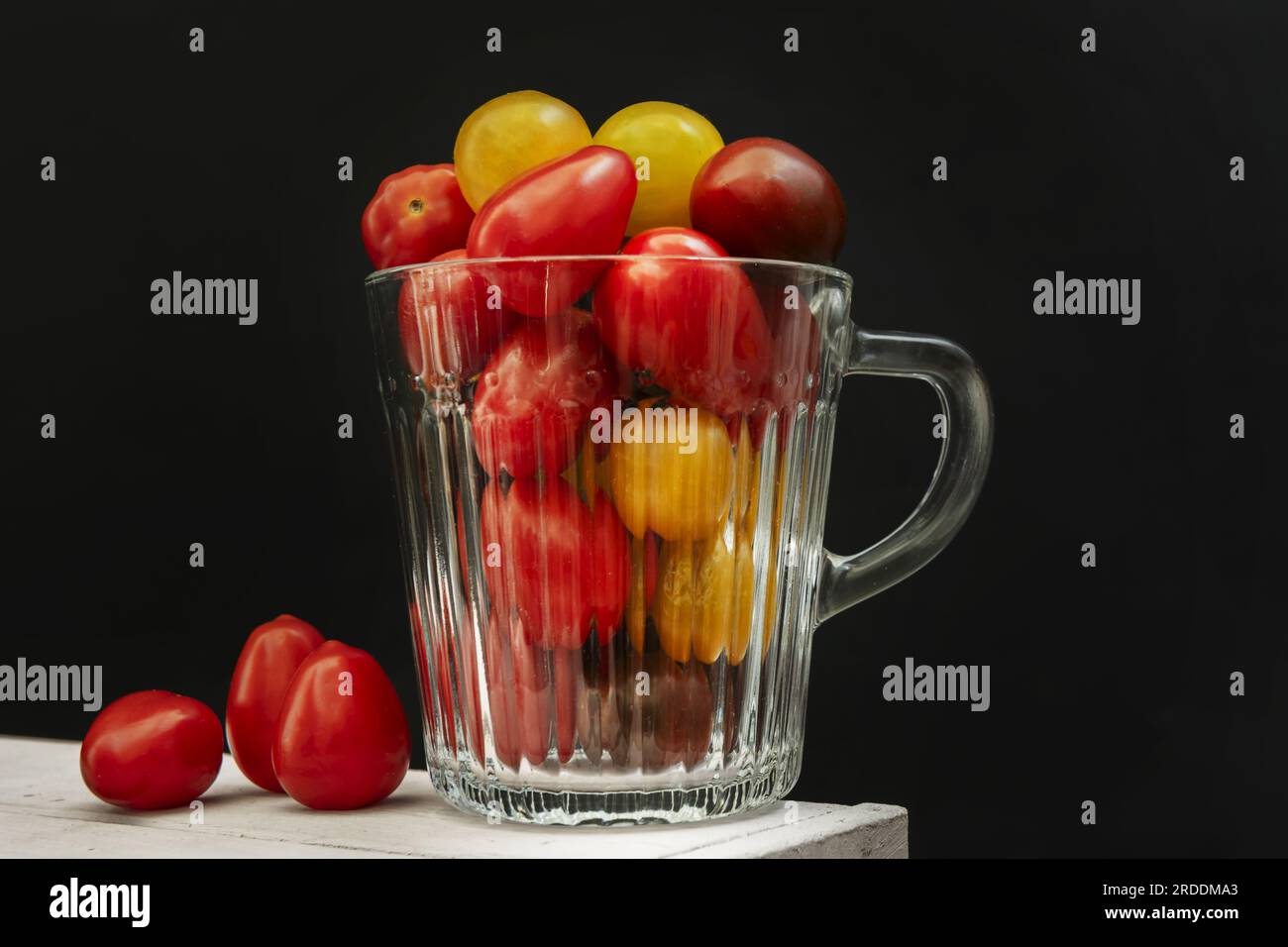 Un piccolo vaso di vetro trasparente riempito con pomodori ciliegini maturi di diverse varietà miste Foto Stock