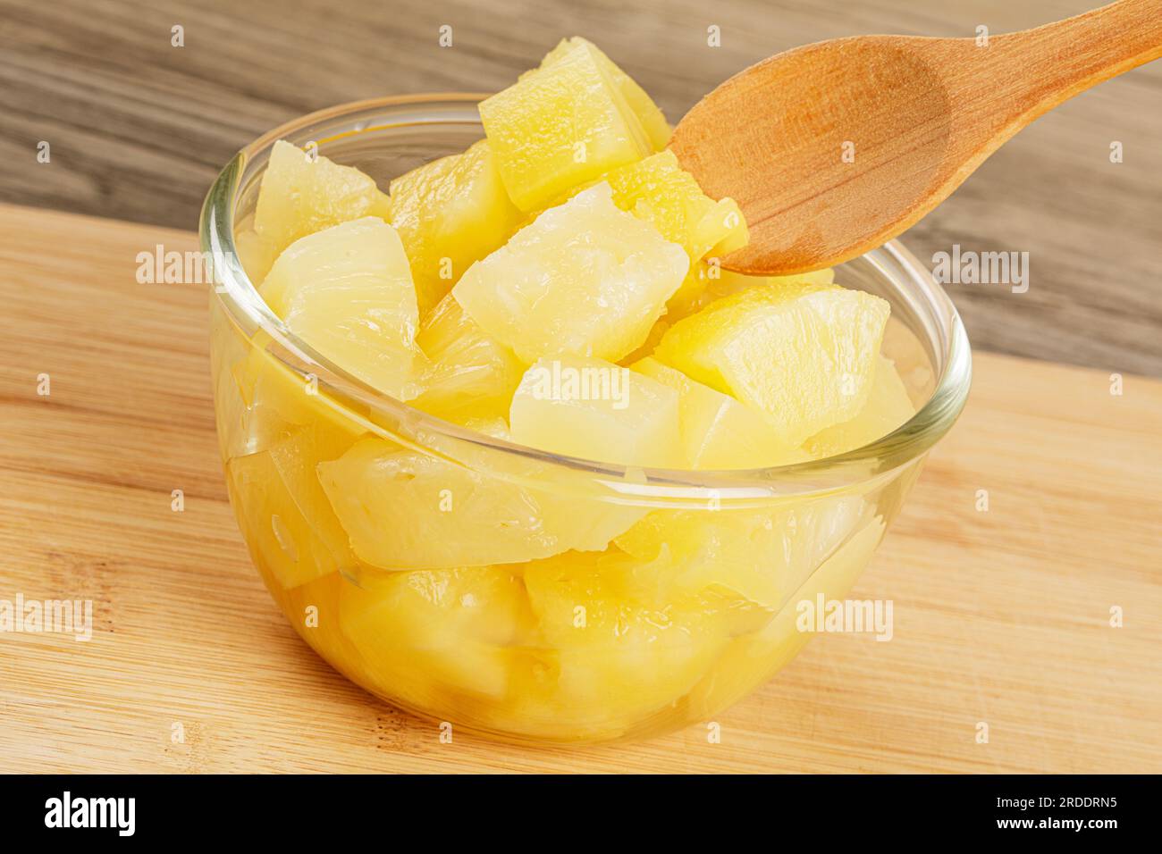 Un primo piano di deliziosi pezzi di ananas è lo sciroppo succoso su uno sfondo di legno con spazio per la copia Foto Stock