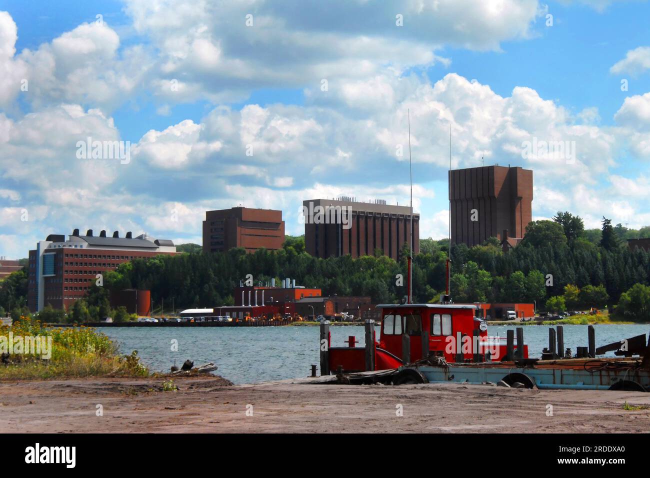 Gli edifici del Michigan Tech Campus sono incorniciati da un cielo blu. La parte anteriore dell'immagine mostra un rimorchiatore rosso brillante attraccato sul lago Portage tra Houghton e. Foto Stock