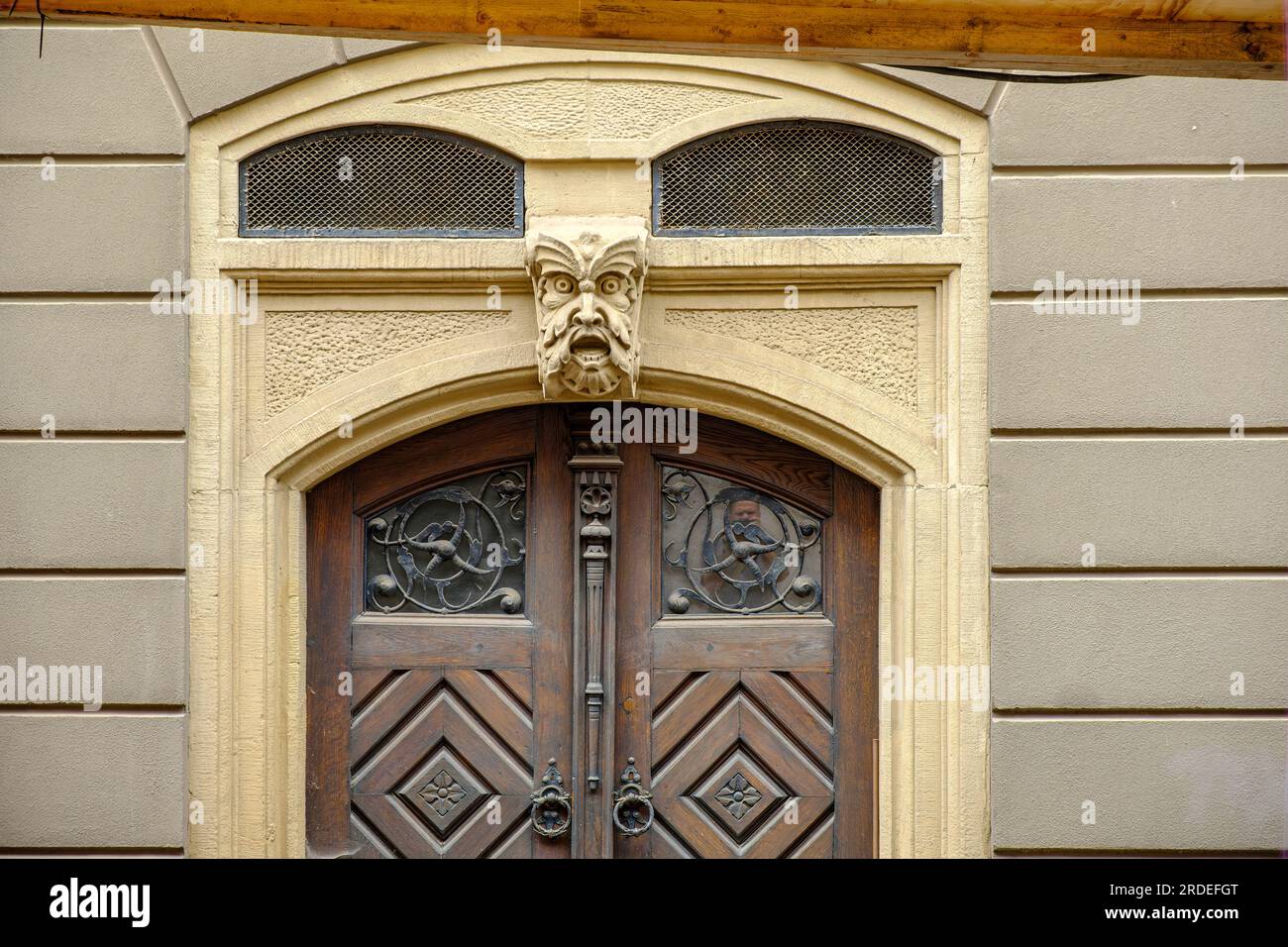 Classico cancello anteriore in legno con una faccia griffata come chiave di volta nell'arco di un edificio storico nel centro storico di Gotha, Turingia, Germania. Foto Stock