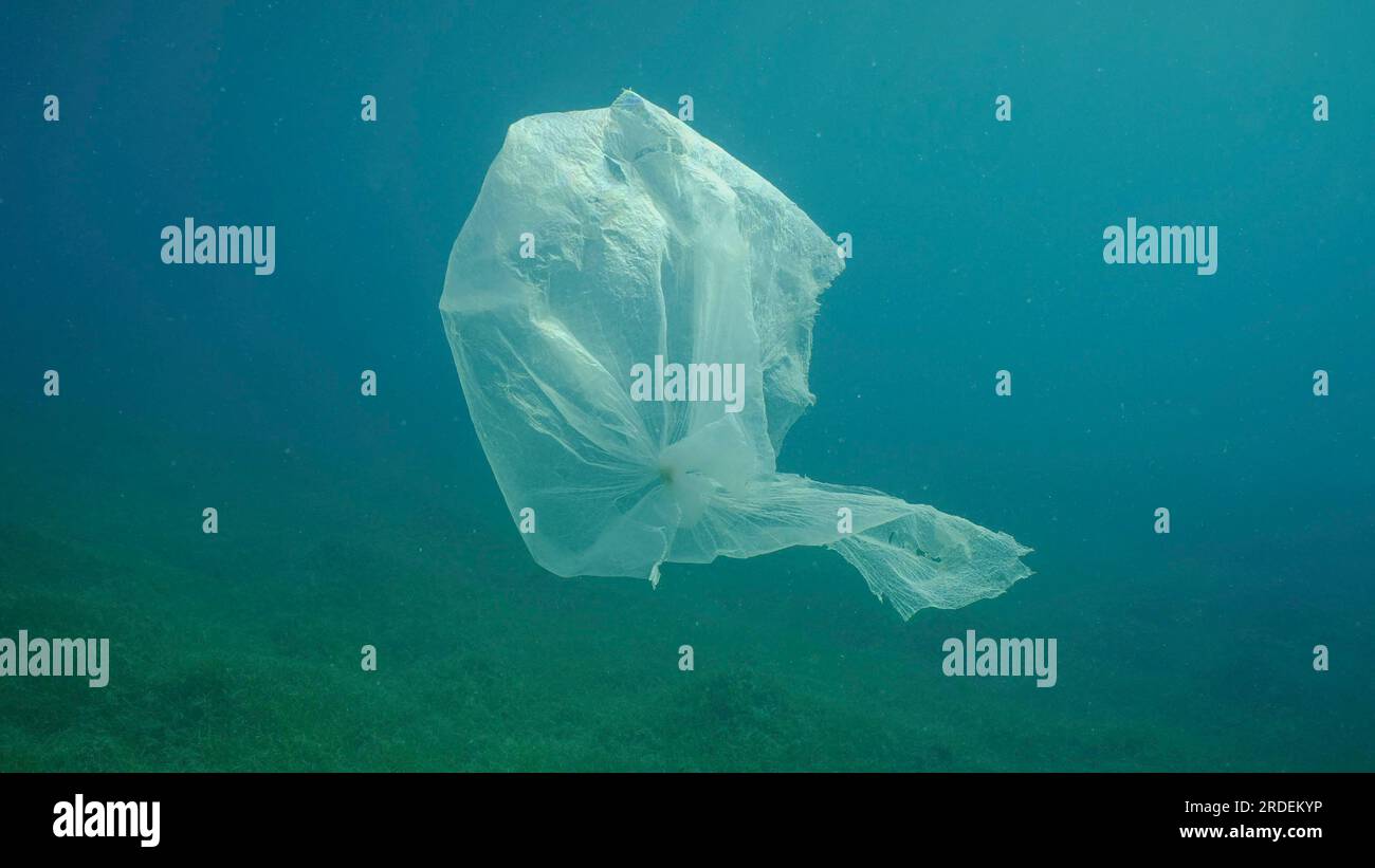 Vecchio sacchetto di plastica che si sposta nella colonna d'acqua sopra il prato di sabbia. Sacchetto di plastica galleggiante sott'acqua sulla profondità blu, inquinamento ambientale. Plastica Foto Stock