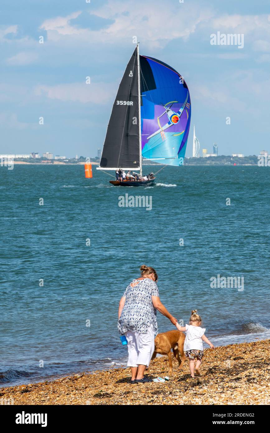 nonna con nipote e cane che camminano insieme lungo una spiaggia di ciottoli al sole a cowes, sull'isola di wight, regno unito Foto Stock