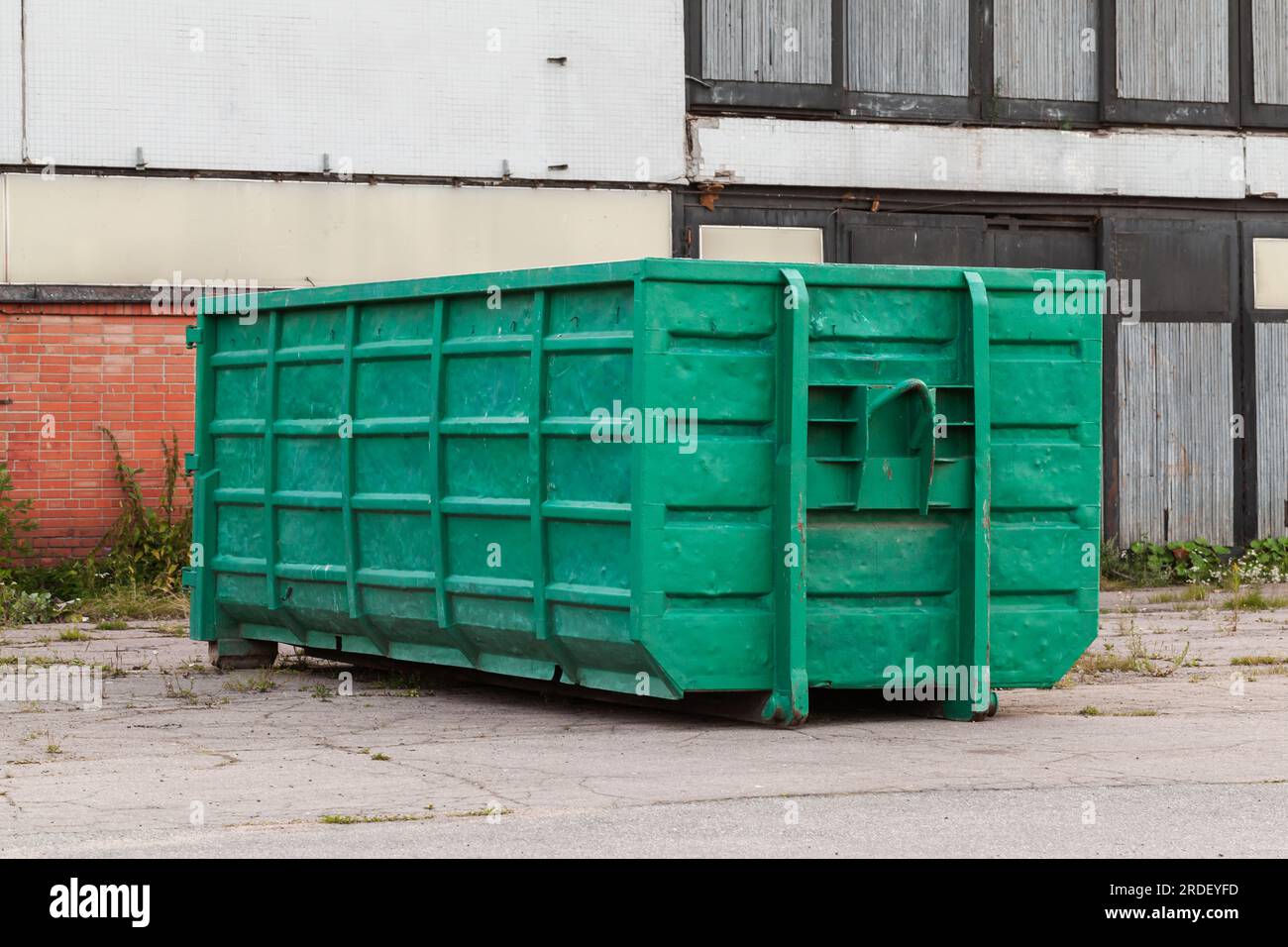 Un grande contenitore per la spazzatura verde si trova in una città vicino a un muro di cemento Foto Stock