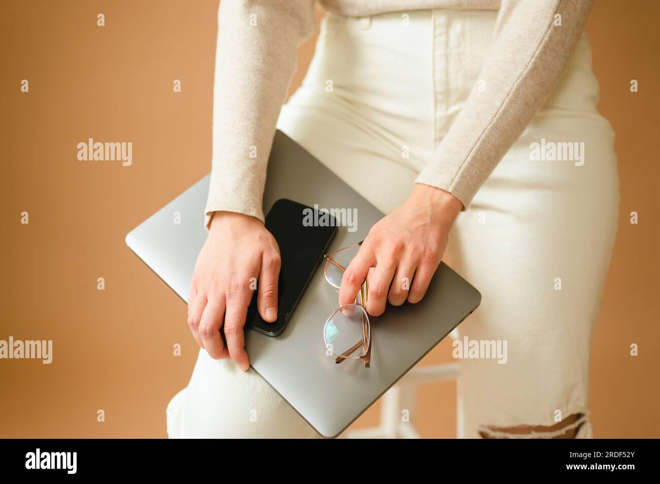 Primo piano di una donna che tiene uno smartphone, un computer portatile e degli occhiali sulla gamba Foto Stock