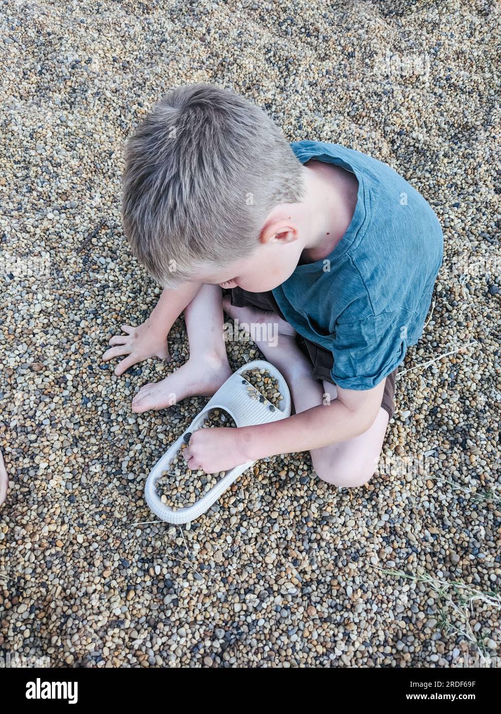 Un ragazzo versa piccoli ciottoli di mare in una ciabatta di gomma Foto Stock