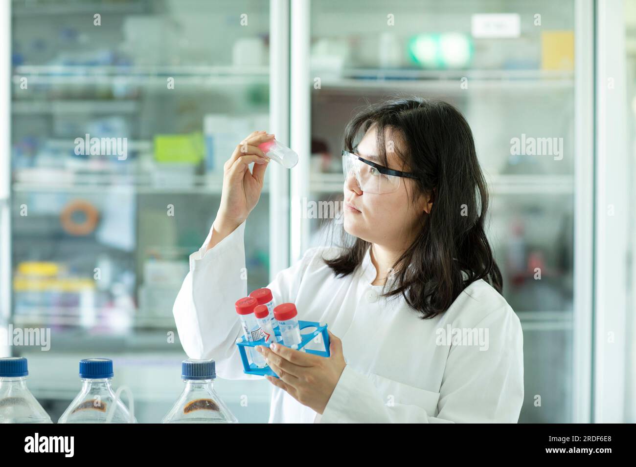 giovane scienziata cinese femmina che controlla un campione in un tubo Foto Stock