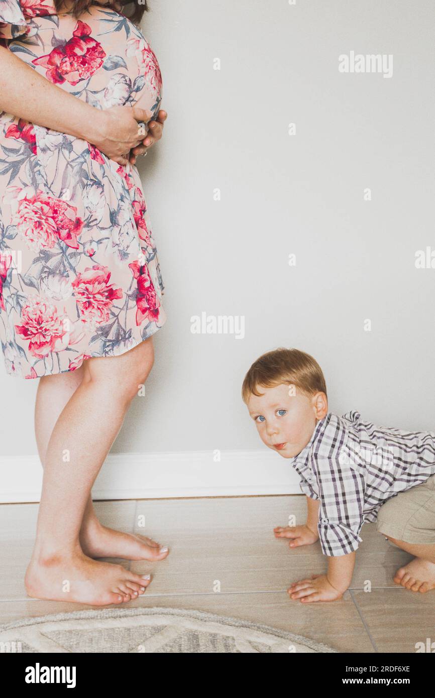 Bambino sul pavimento di fronte alla mamma incinta Foto Stock