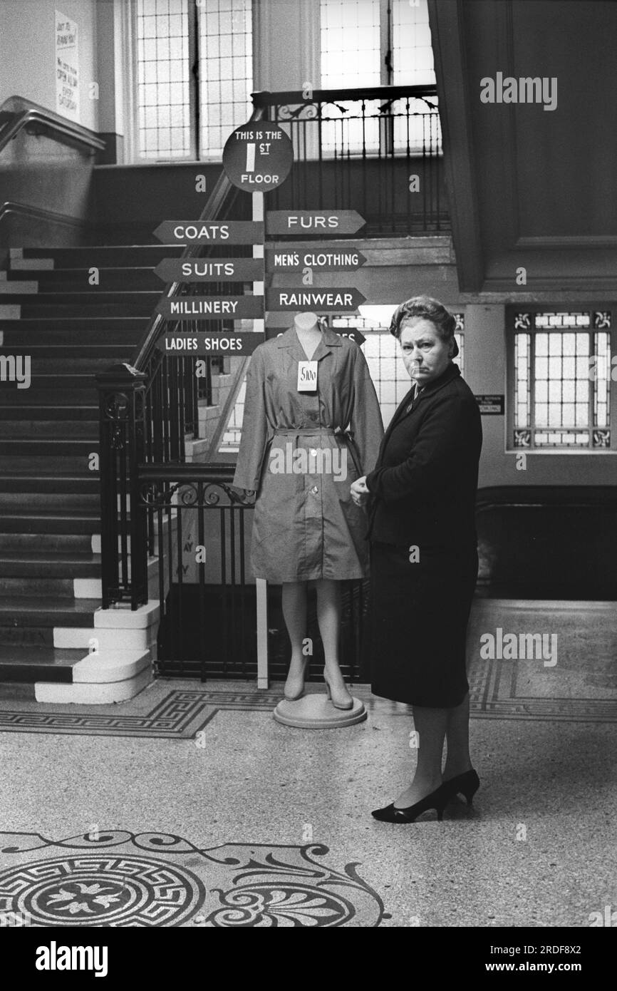Grandi magazzini 1960s Regno Unito. Derry e Toms, i grandi magazzini di Kensington High Street. Londra, l'atterraggio delle scale con il cartello di direzione Cappotti, Furs, Suit, abbigliamento da pioggia, scarpe da donna, fresatura. Inghilterra 1968. REGNO UNITO HOMER SYKES Foto Stock