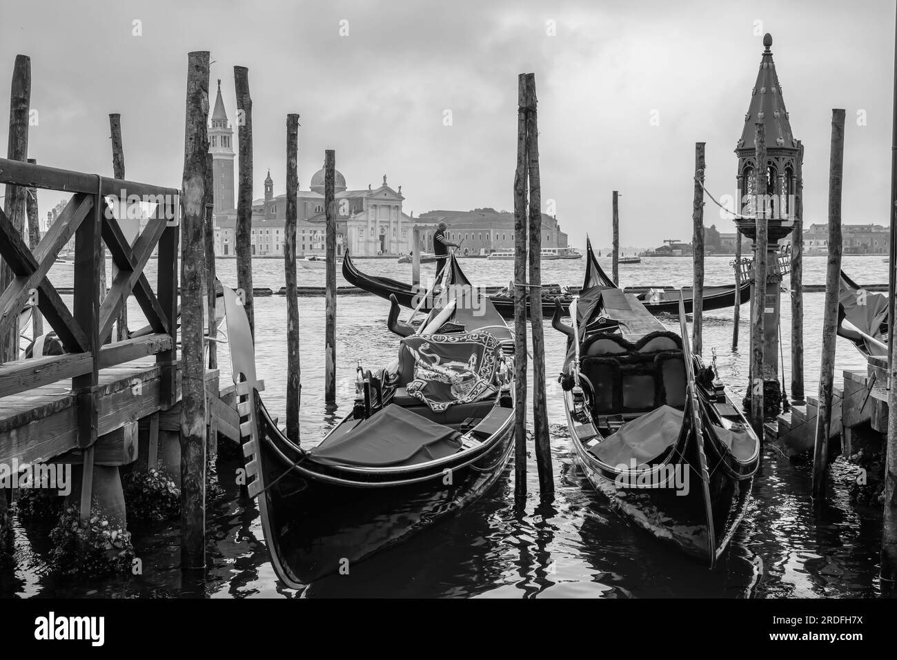 Venezia, Italia - 27 aprile 2019 : Un molo di legno con lanterna, gondole e un gondoliere che passa sullo sfondo a Venezia Italia in bianco e nero Foto Stock