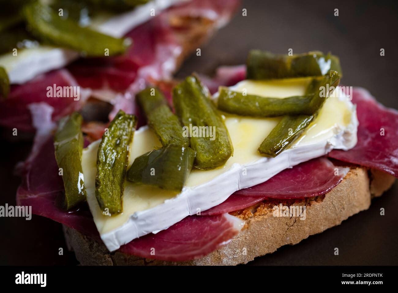 Pintxo di prosciutto iberico, formaggio brie, confit di peperoni verdi Foto Stock
