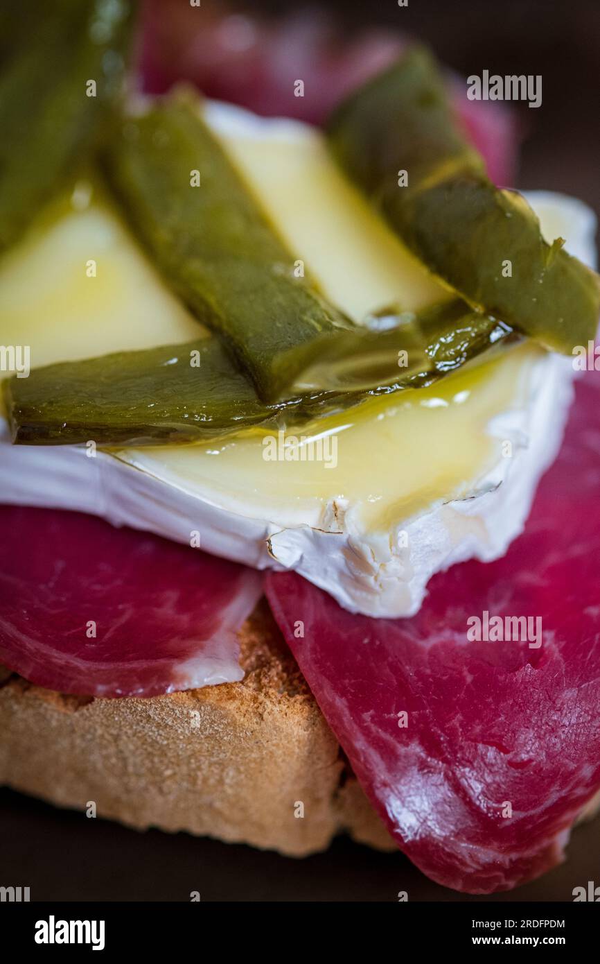 Pintxo di prosciutto iberico, formaggio brie, confit di peperoni verdi Foto Stock