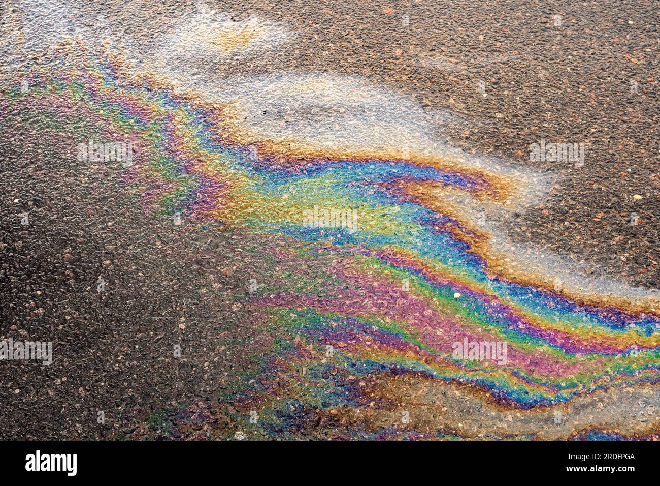 Le pozzanghere sono contaminate da flussi di olio multicolore. Macchia d'olio sull'asfalto, macchia di benzina colorata a forma di arcobaleno su una strada asfaltata come un te Foto Stock