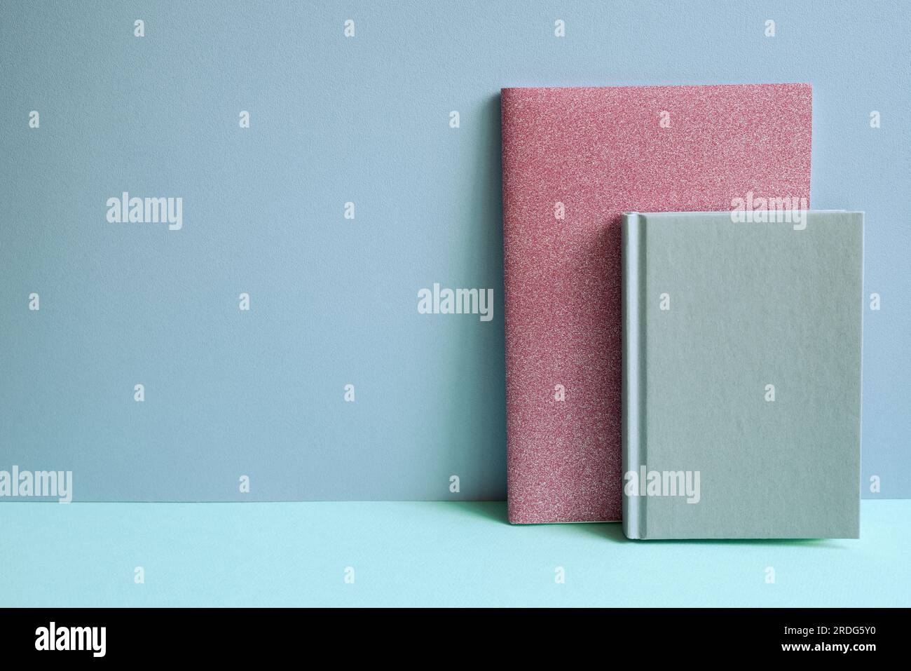 Notebook rosa su scrivania blu. sfondo a parete blu Foto Stock