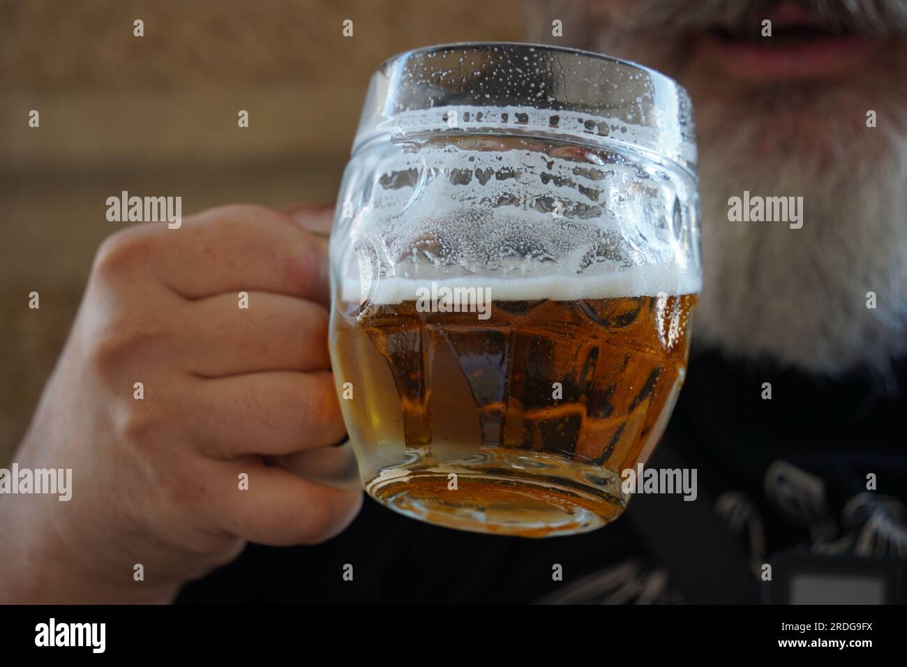 Un uomo che beve birra. Un uomo con la barba che beve una tazza di birra al pub Foto Stock