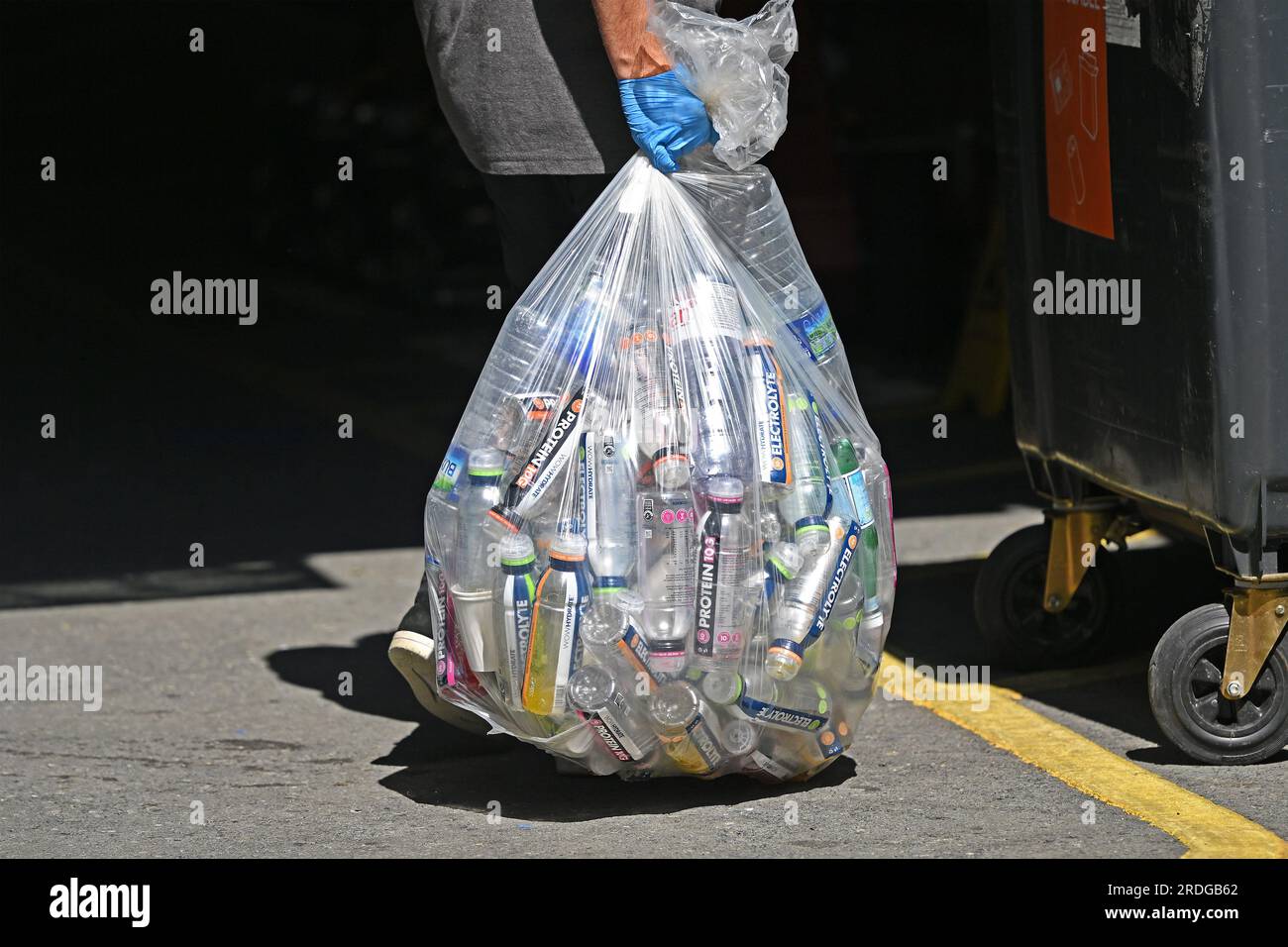 Un operaio porta un sacchetto di plastica pieno di bottiglie di plastica vuote a Fulham, nel sud di Londra. 21 luglio 2023. Foto Stock