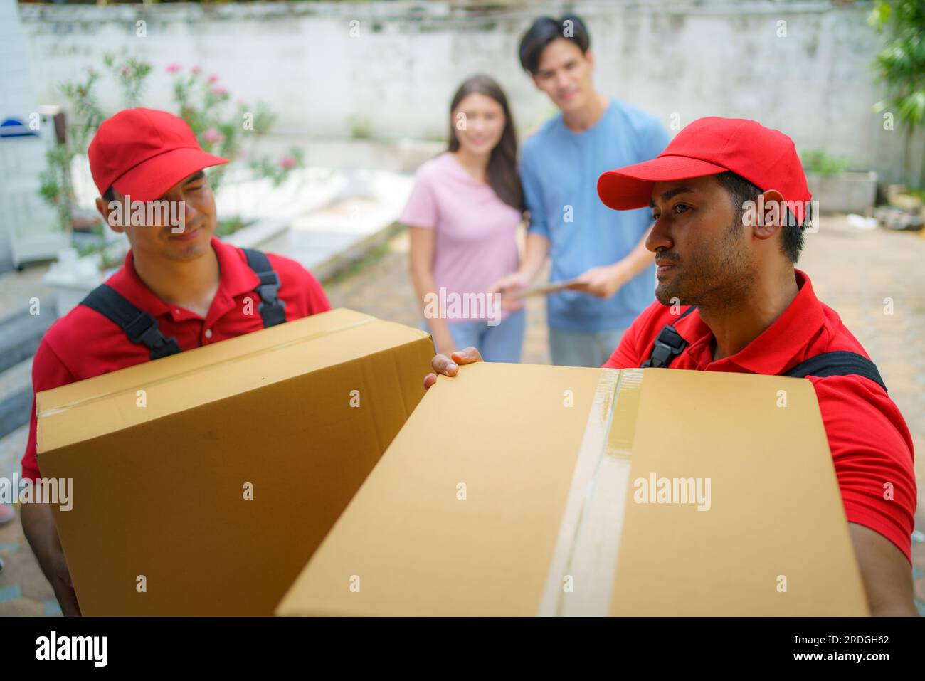 Una coppia asiatica sta insieme, osservando con anticipazione mentre i lavoratori si trasferiscono nella loro nuova casa. L'eccitazione riempie l'aria mentre si aspettano con ansia Foto Stock