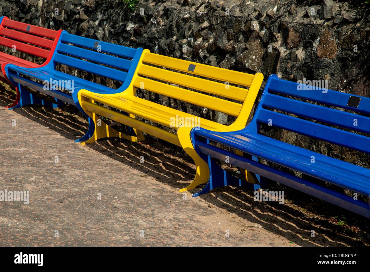 Panchine pubbliche di colori assortiti su una parete di un passaggio pedonale sulla spiaggia Foto Stock