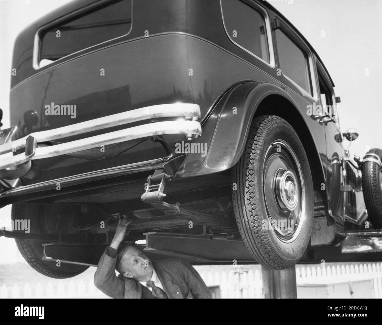 Pasadena, California: c. 1926 Un uomo che ispeziona l'assale posteriore di una nuova auto su un ascensore. Il differenziale è stato spostato nella parte anteriore per consentire alla vettura di sedersi più in basso a terra e di eliminare i predellini. Non si sa ancora quando la misteriosa vettura a trazione anteriore entrerà in produzione. Foto Stock