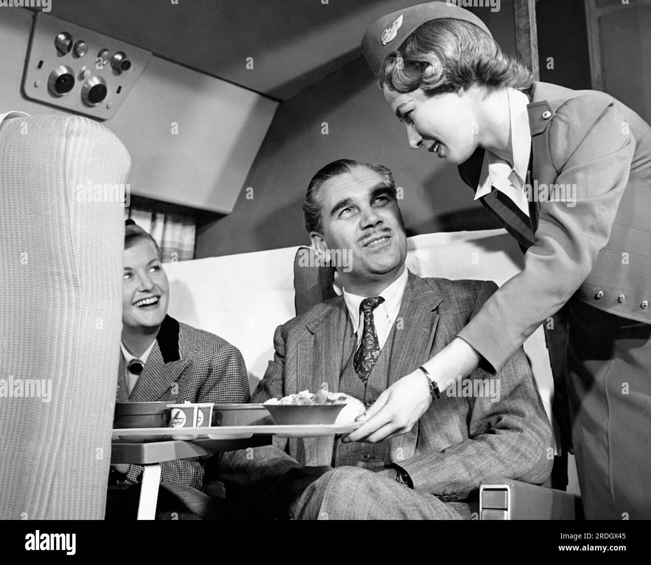 Stati Uniti: c. 1953 Una hostess di Capital Airlines serve cibo e bevande a due passeggeri. Foto Stock