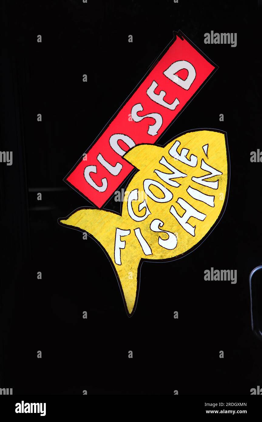 La porta di vetro del caffè ha un cartello che dice CLOSED Gone Fishin. È possibile vedere la maniglia della portiera e le barre metalliche all'interno della portiera. Il segno è che ha un pesce giallo. Foto Stock
