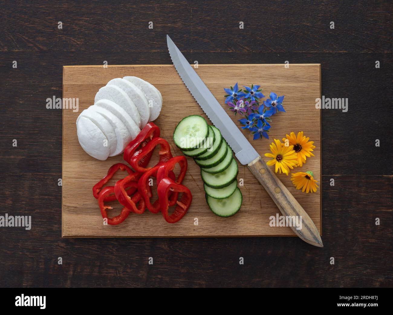 Preparazione dell'insalata con mozarella, peperone, cetriolo e fiori commestibili selvatici calendula e borragine Foto Stock