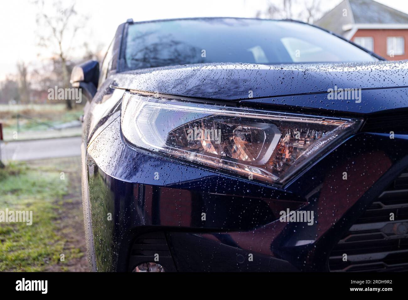 Un ritratto ravvicinato del faro sinistro di un'auto ibrida toyota rav4 blu scuro parcheggiata su un vialetto. Il veicolo può guidare elettricamente e su fossili Foto Stock