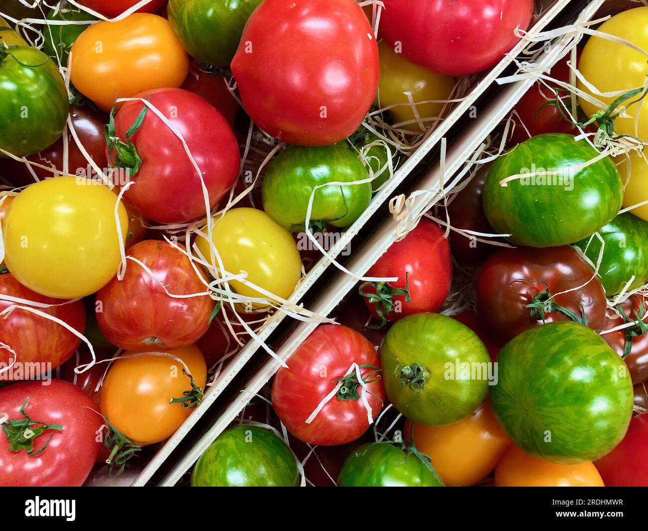 Pomodori coltivati biologici freschi, di diversi colori e sapori, posti in scatole di legno in vendita al mercato agricolo. Foto Stock