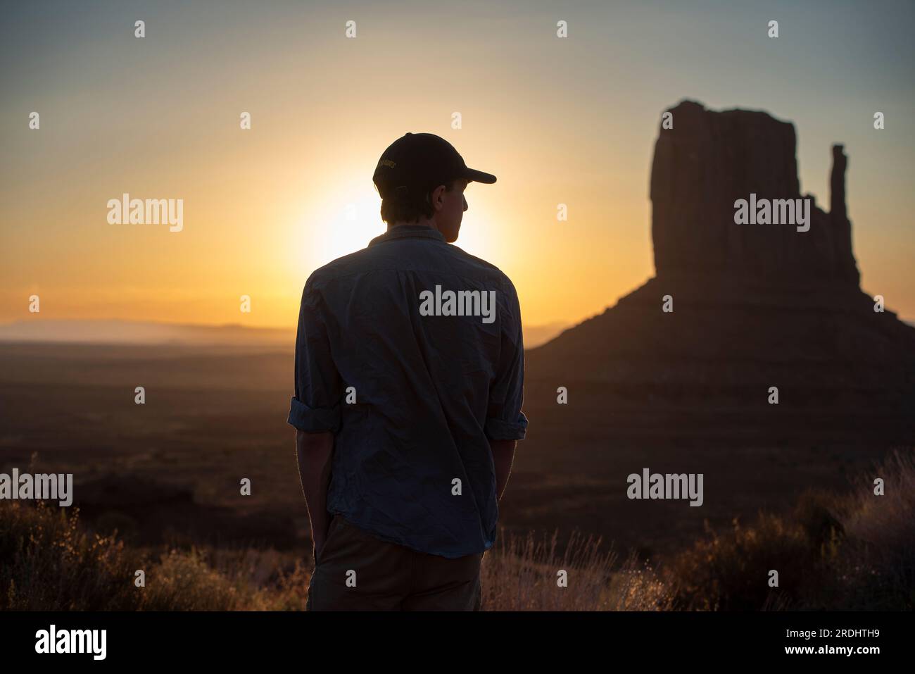 Un giovane, retroilluminato, sta osservando l'alba a Monument Valley, Arizona, con uno dei Mittens alla sua destra. Foto Stock