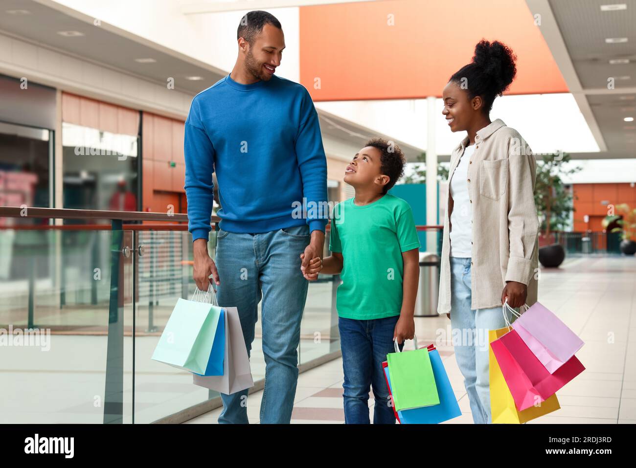Shopping per famiglie. Genitori e figlio felici con borse colorate nel centro commerciale Foto Stock