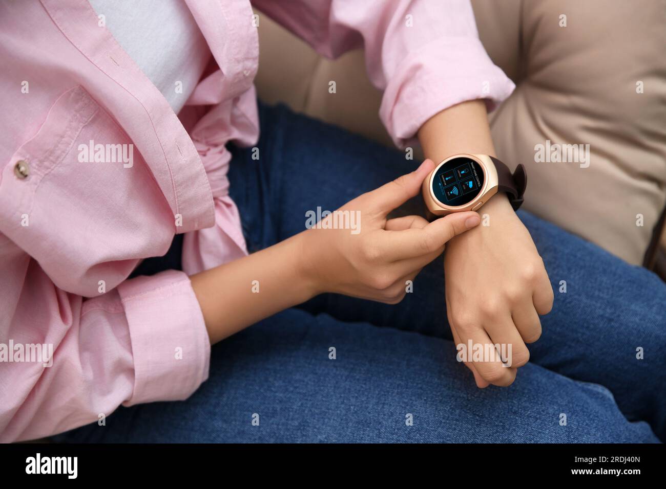 Donna che imposta il sistema di controllo della casa intelligente tramite smartwatch al chiuso, primo piano. Interfaccia app con icone sul display Foto Stock