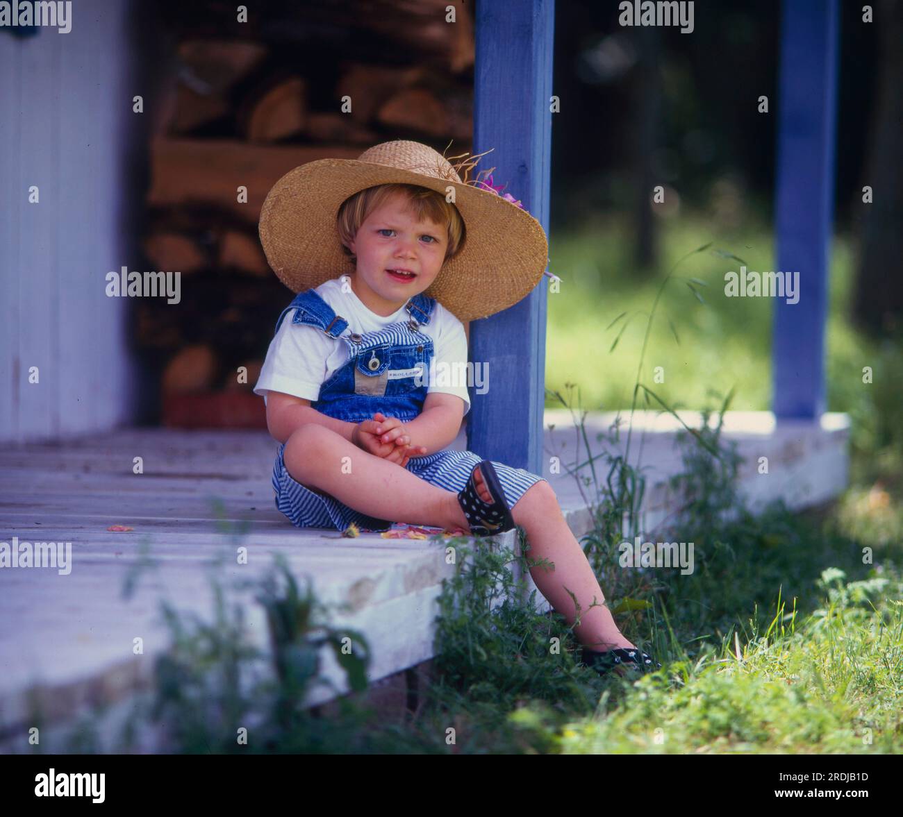 Bambina con cappello da sole seduta su una veranda di legno Foto Stock