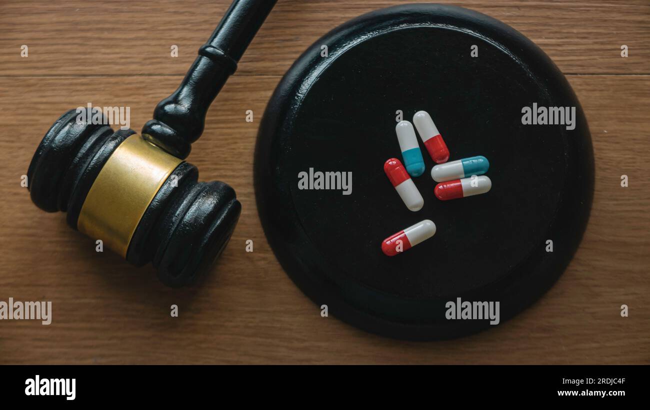 Farmaci, medicina, farmaceutica e concetto di legge. Gavel e pillole su una scrivania di legno. Foto Stock