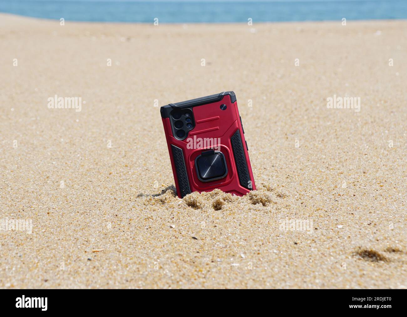 Uno smartphone rosso mezzo sepolto nella sabbia sulla spiaggia Foto Stock