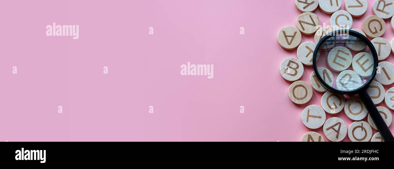 Concetto di apprendimento dell'inglese, ricerca di parole e informazioni. Lettera alfabetica inglese e lente di ingrandimento. Sfondo rosa con spazio di copia. Foto Stock
