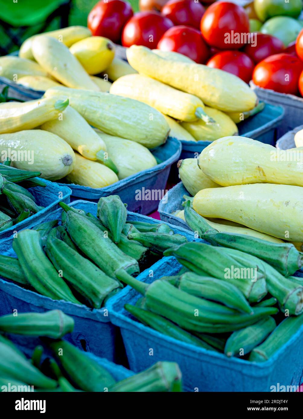 Sfondo alimentare di okra fresca, zucca gialla a collo di cocco e pomodori esposti in un mercato di prodotti. Foto Stock