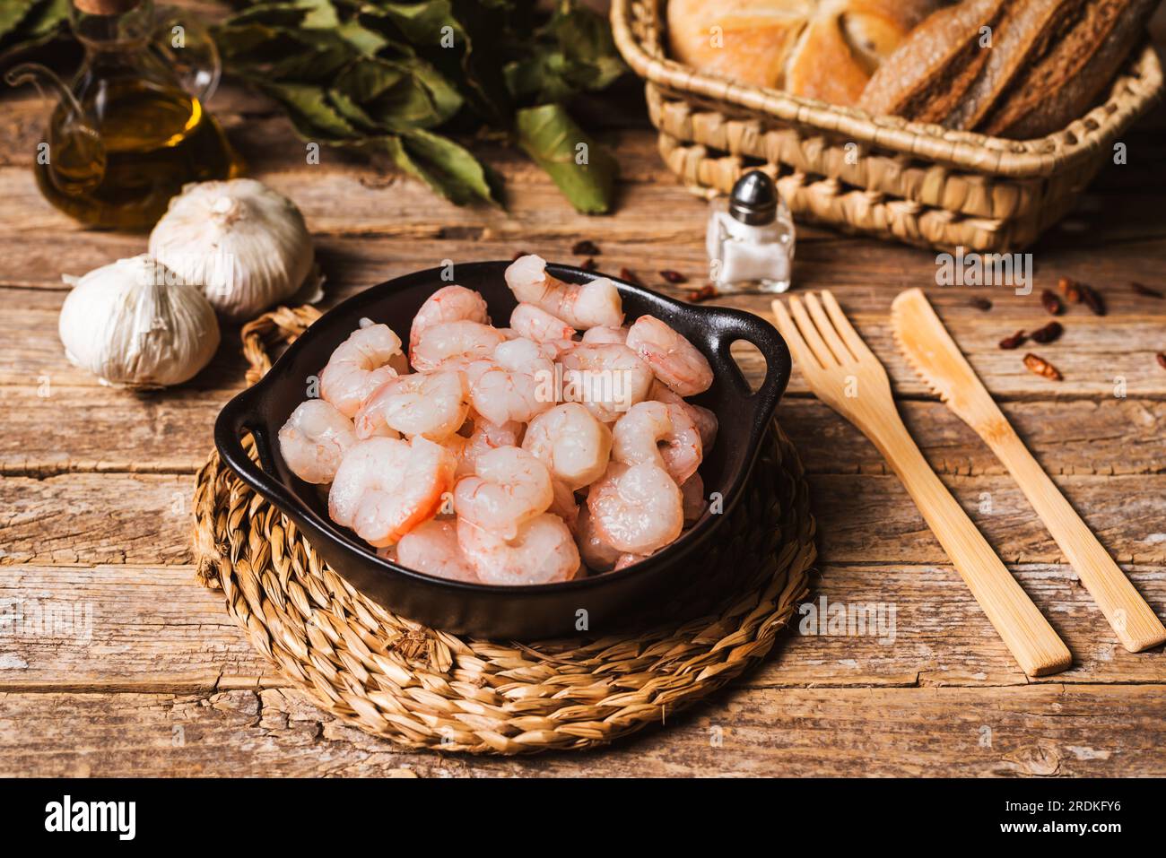 Gamberoni crudi su un piatto su un tavolo rustico, con gli ingredienti per prepararli con l'aglio. Foto Stock