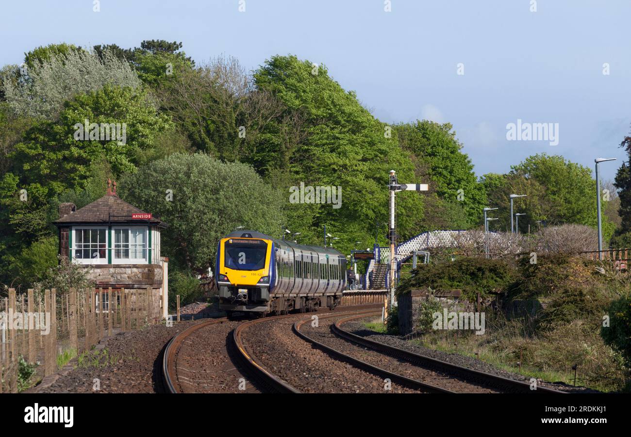 Treno Northern Rail classe 195 ad Arnside che passa per la scatola di segnalazione meccanica della Furness Railway e un segnale di casa del semaforo Foto Stock