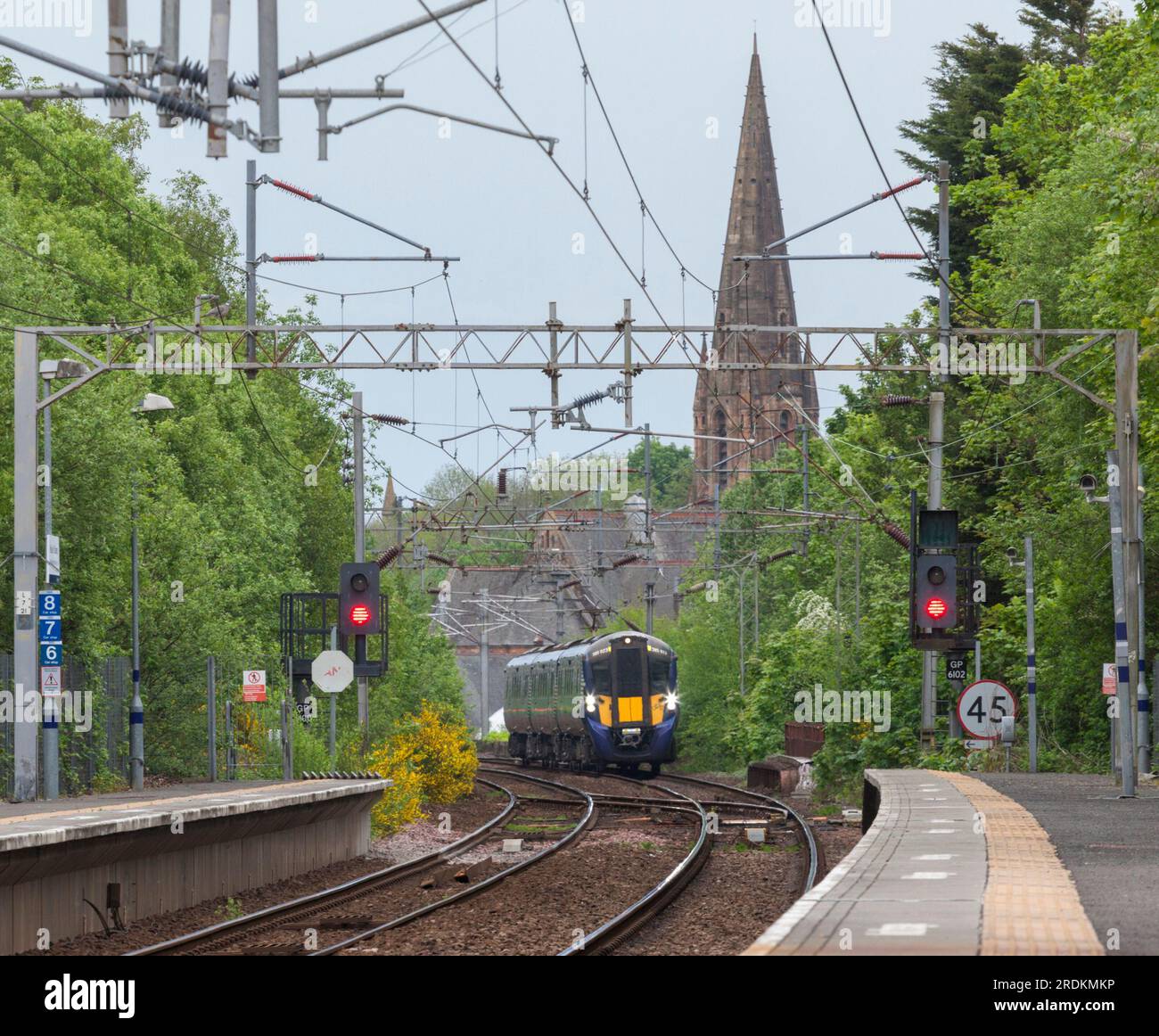 Treno elettrico a più unità ScotRail Siemens classe 385 che arriva alla stazione ferroviaria di Paisley St James con la guglia della chiesa di Paisley St James alle spalle Foto Stock