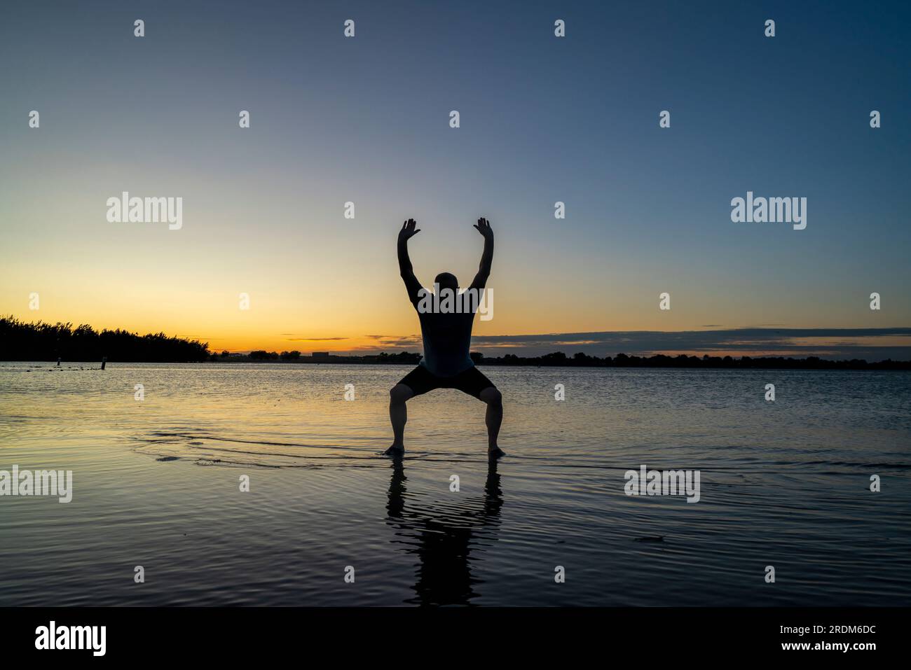 Sunrise silhouette di un uomo in piedi in acqua poco profonda e la pratica di chigong o tai chi movimenti, Boyd il lago del Parco statale nel nord del Colorado Foto Stock