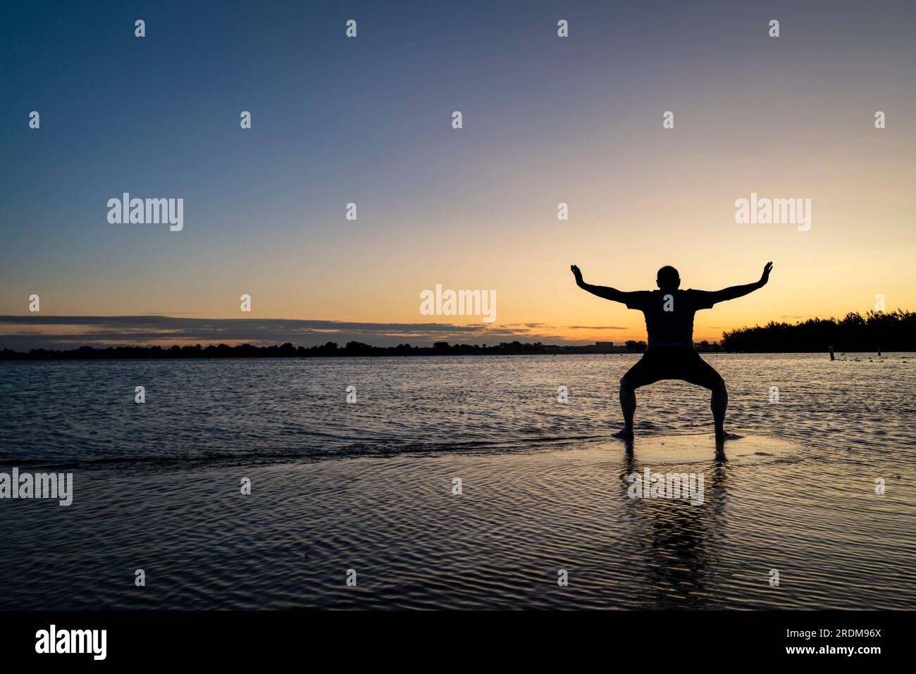 Sunrise silhouette di un uomo in piedi in acqua poco profonda e la pratica di chigong o tai chi movimenti, Boyd il lago del Parco statale nel nord del Colorado Foto Stock