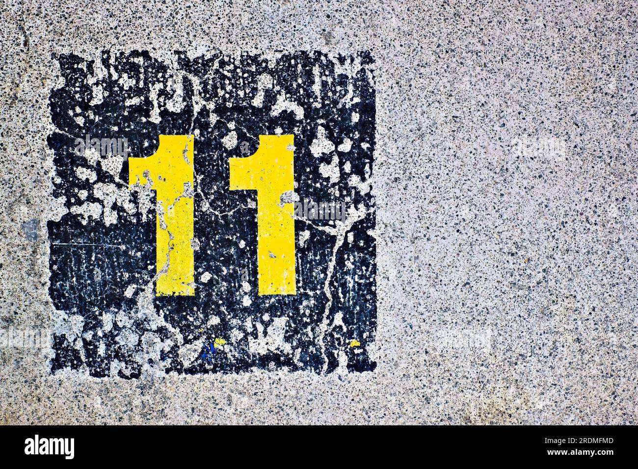 Giallo numero 11, undici, in quadrato blu scuro, sfalsato su una superficie piana in calcestruzzo. Foto Stock